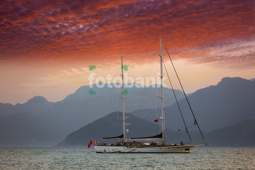 A Boat Sailing in the sea with Mountains Red clouds in the Sky