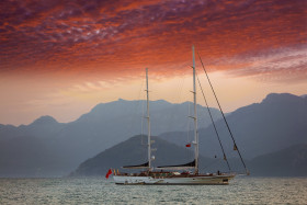 A Boat Sailing in the sea with Mountains Red clouds in the Sky