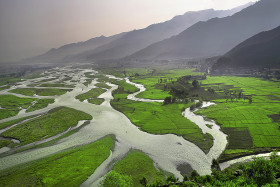 Lush Green field and river flowing under the Mountains